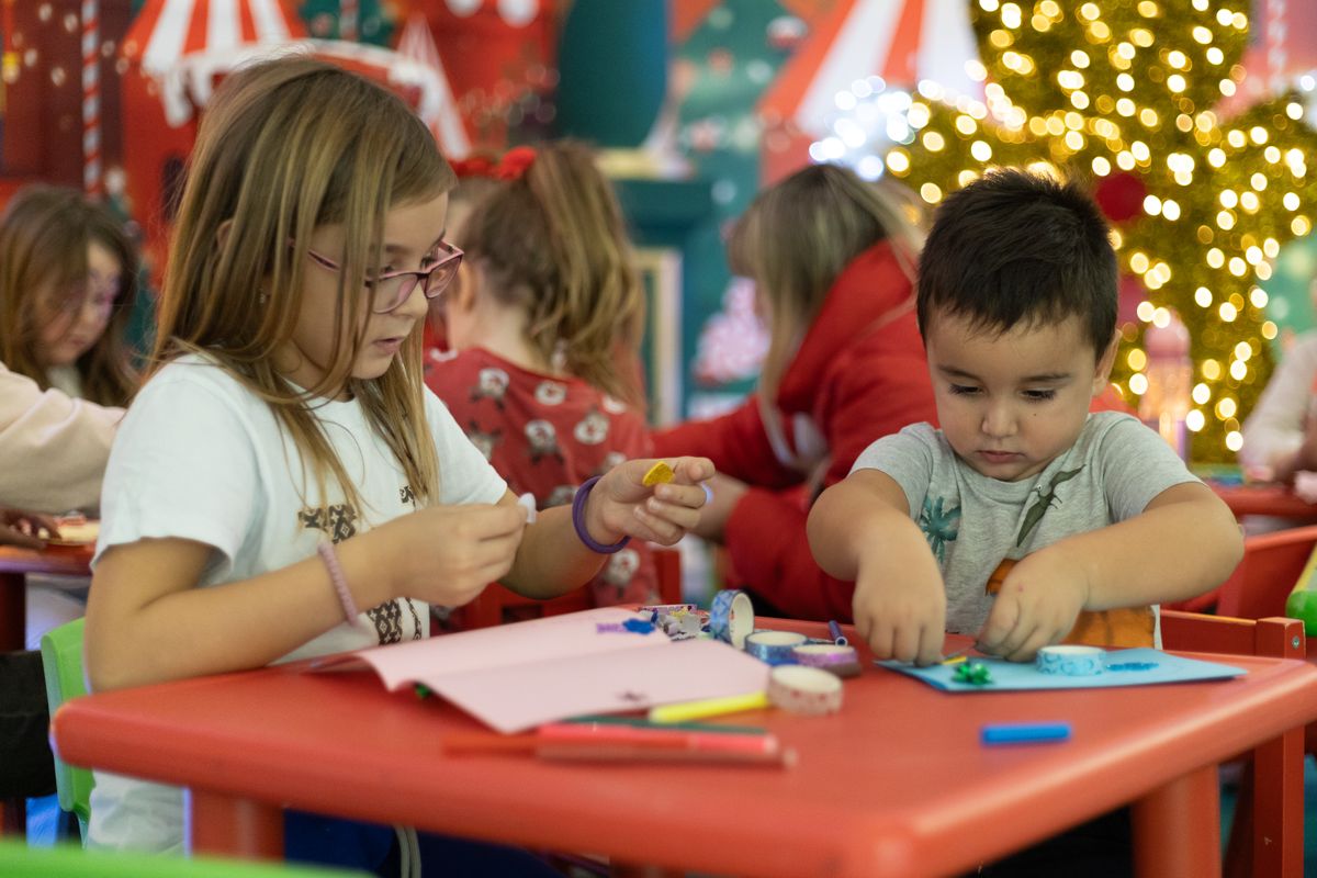 Enfants et parents penchés sur une table couverte de matériaux de bricolage de Noël colorés