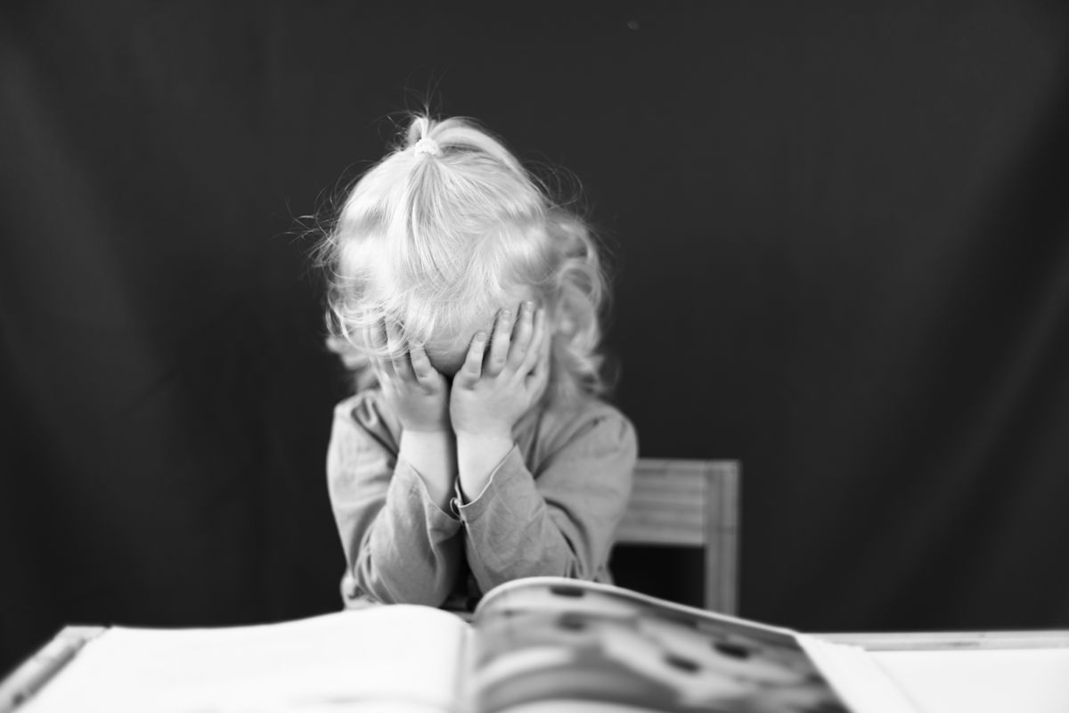 Enfant lisant avec difficulté un livre illustré, accompagné d'un adulte bienveillant