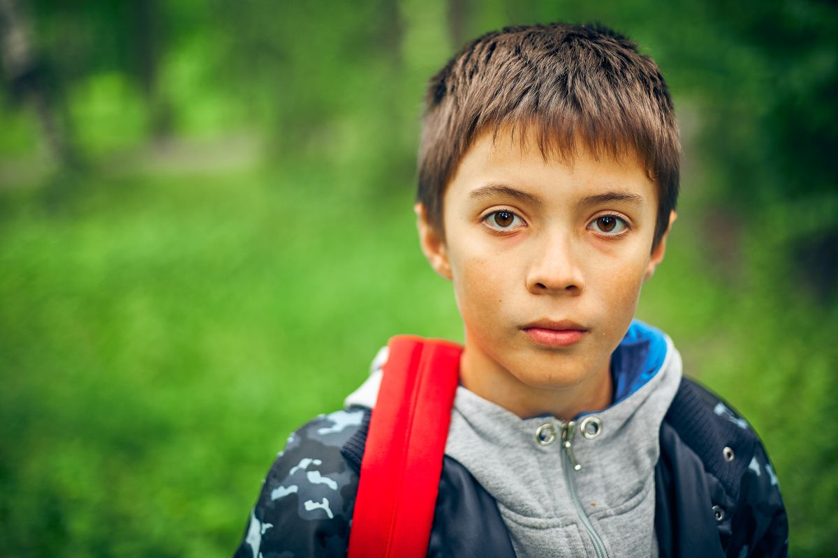 Enfant anxieux devant la grille de l'école, sac sur le dos, parent à ses côtés