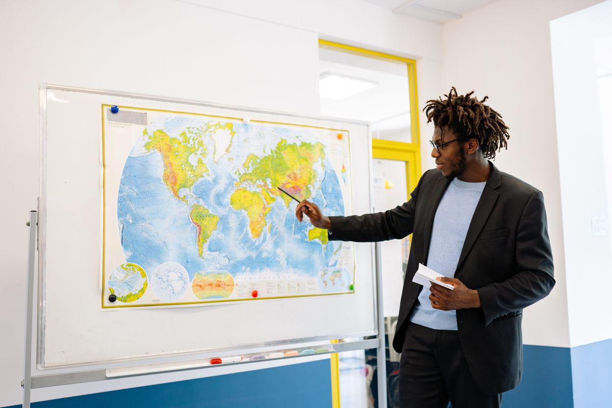 Enseignant pointant une carte murale du monde pendant un cours de géographie en classe
